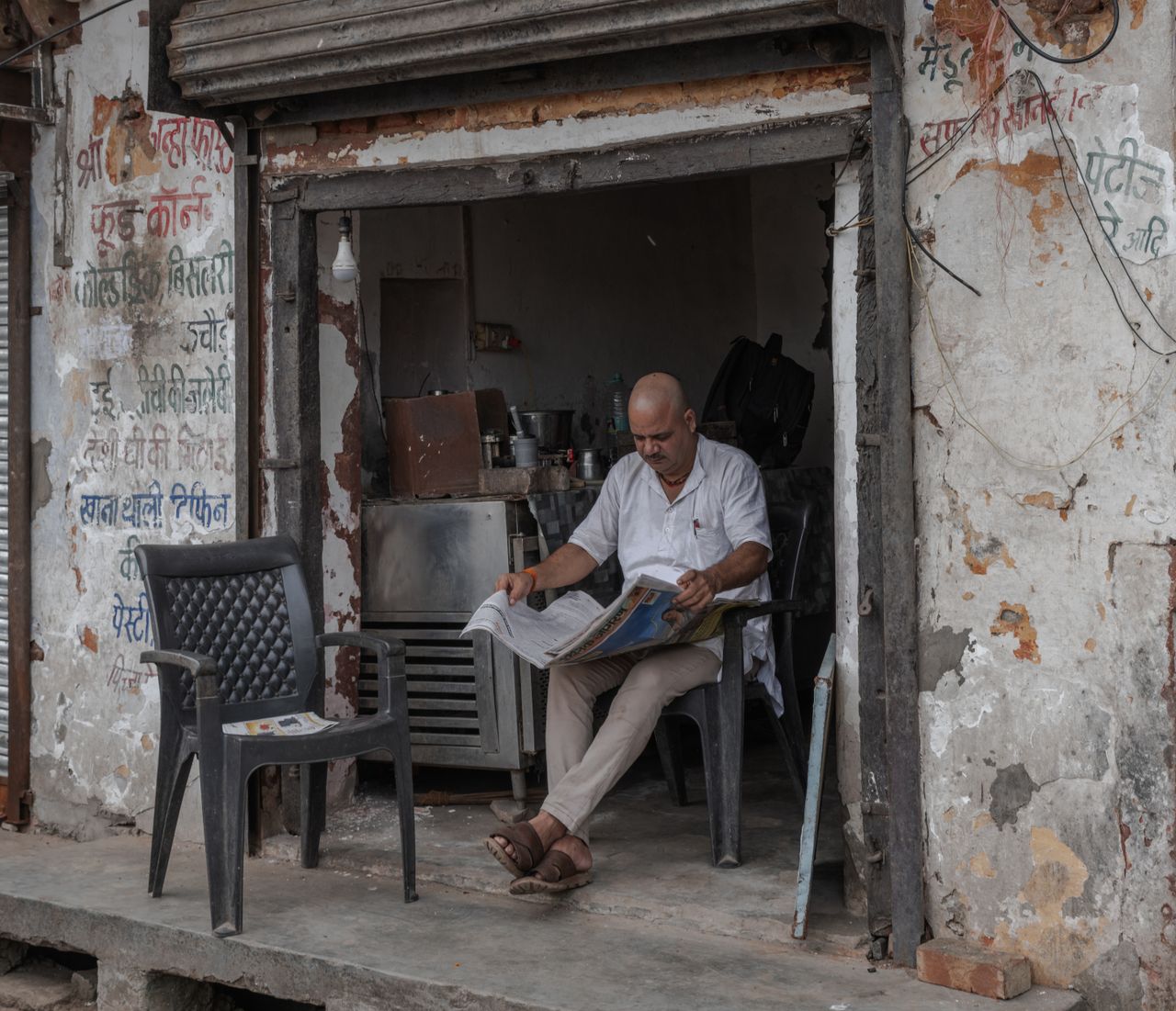 A man relaxes while reading a newspaper outside a rustic cafe in Mathura, India.